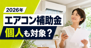 「2026年 エアコン補助金 個人も対象？」の文字と、エアコンのある室内でスマートフォンと書類を持つ女性